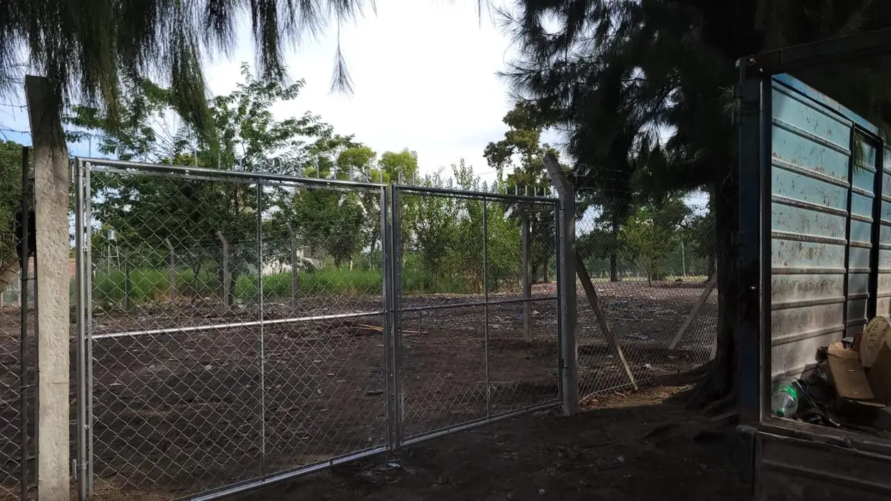 Portón de dos hojas de caño abierto, colocado en un terreno arbolado, con el alambrado de tejido y los hilos de púa arriba a los costados