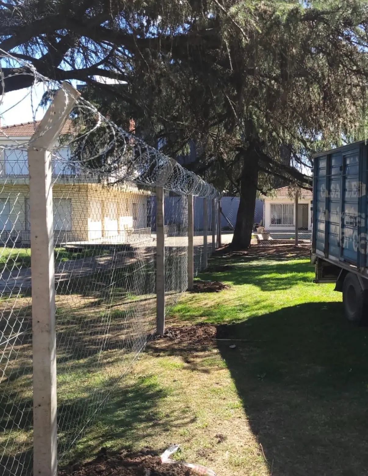 Alambrado olímpico con postes de hormigón curvados y concertina arriba, instalado por Casa Ledesma en el jardín de una casa, con el camión del negocio al lado
